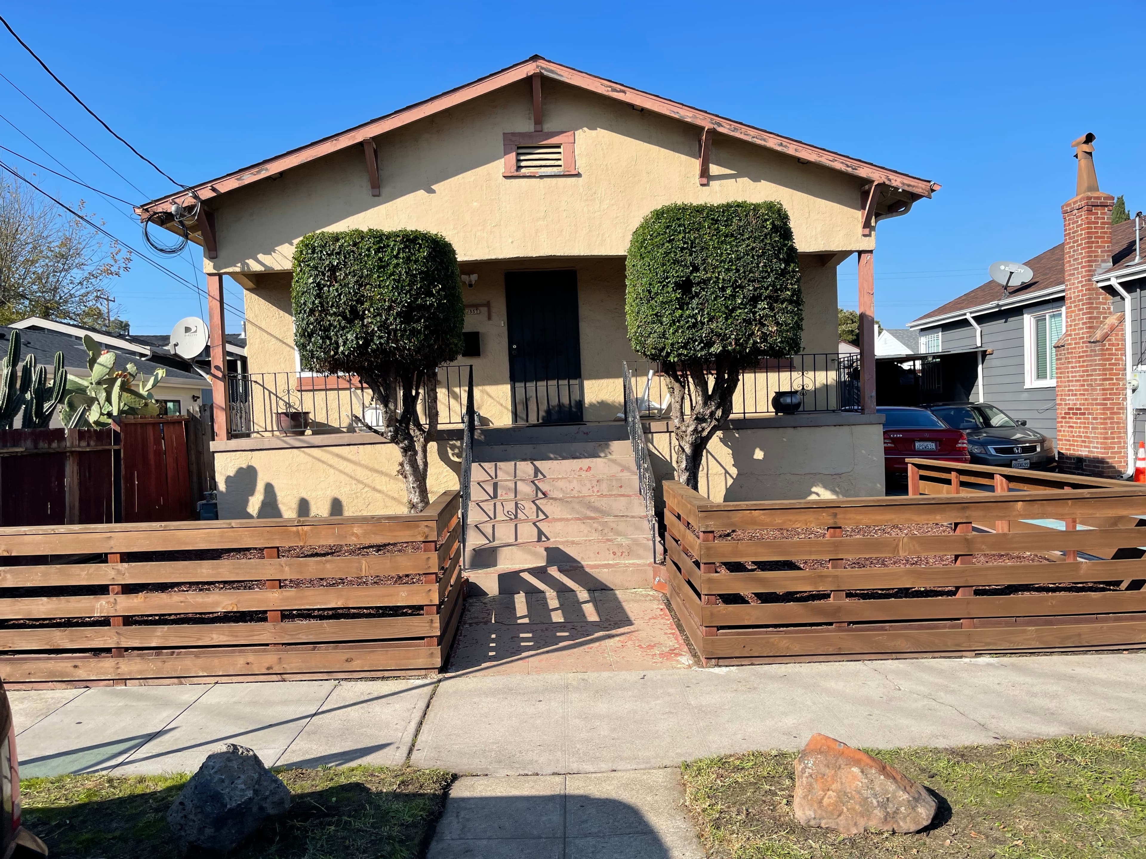Upside-down view of a yellow stucco house with two square-trimmed bushes and a wooden fence.